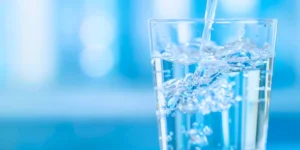 Glass of drinking water filling up, with splashes and bubbles against a soft blue background.